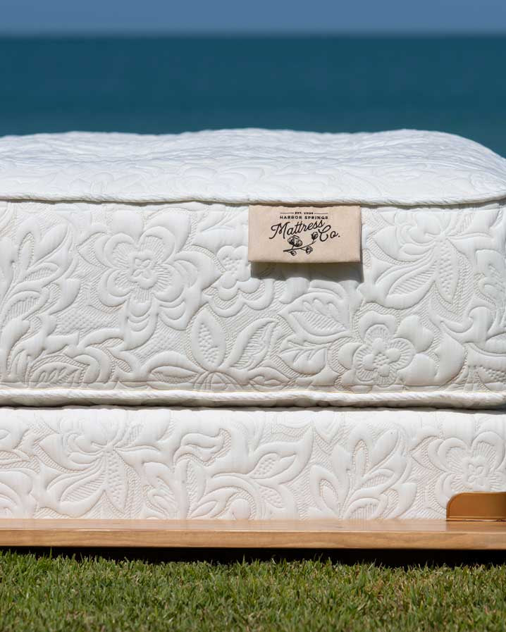 picture of mattress on the grass at Lake Michigan with the water in the background and the harbor springs mattress company logo visable.