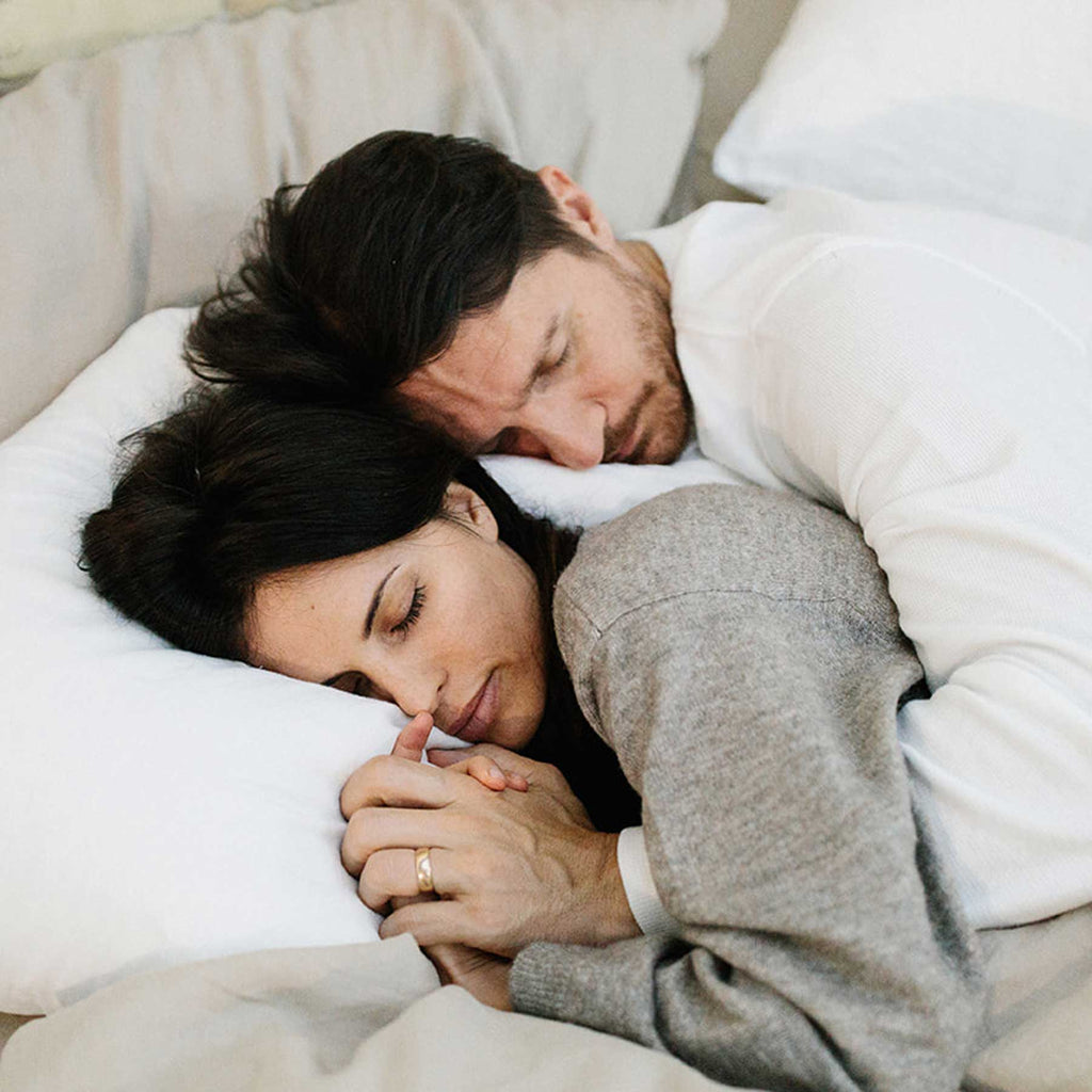 Couple sleeping on a luxury mattress with all natural white and beige linen sheets.