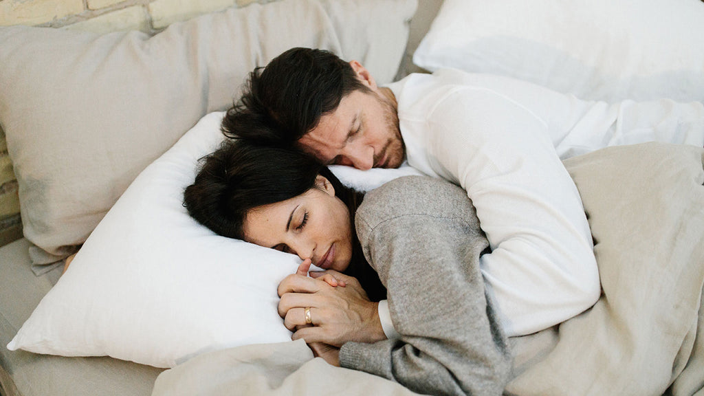 Couple sleeping on a natural luxury mattress on white and beige linen sheets.