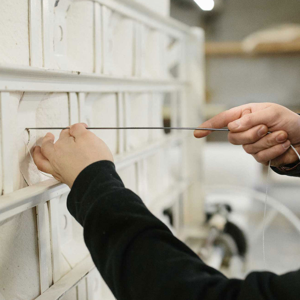 Hands in motion hand-tufting a natural mattress at Harbor Springs Mattress Factory.