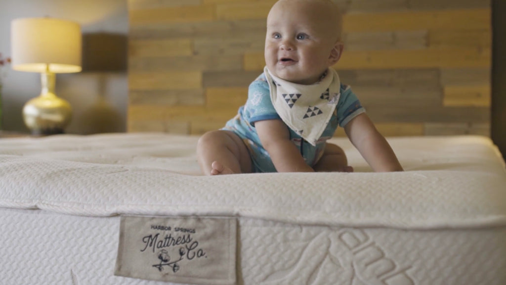 baby smiling and sitting up on a natural latex mattress by harbor springs mattress company.