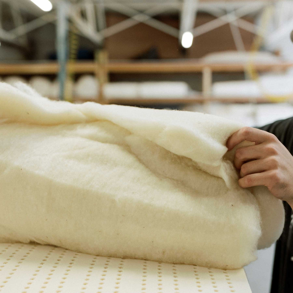 wool batting being rolled out on top of natural latex in mattress making at Harbor Springs Mattress Workshop.