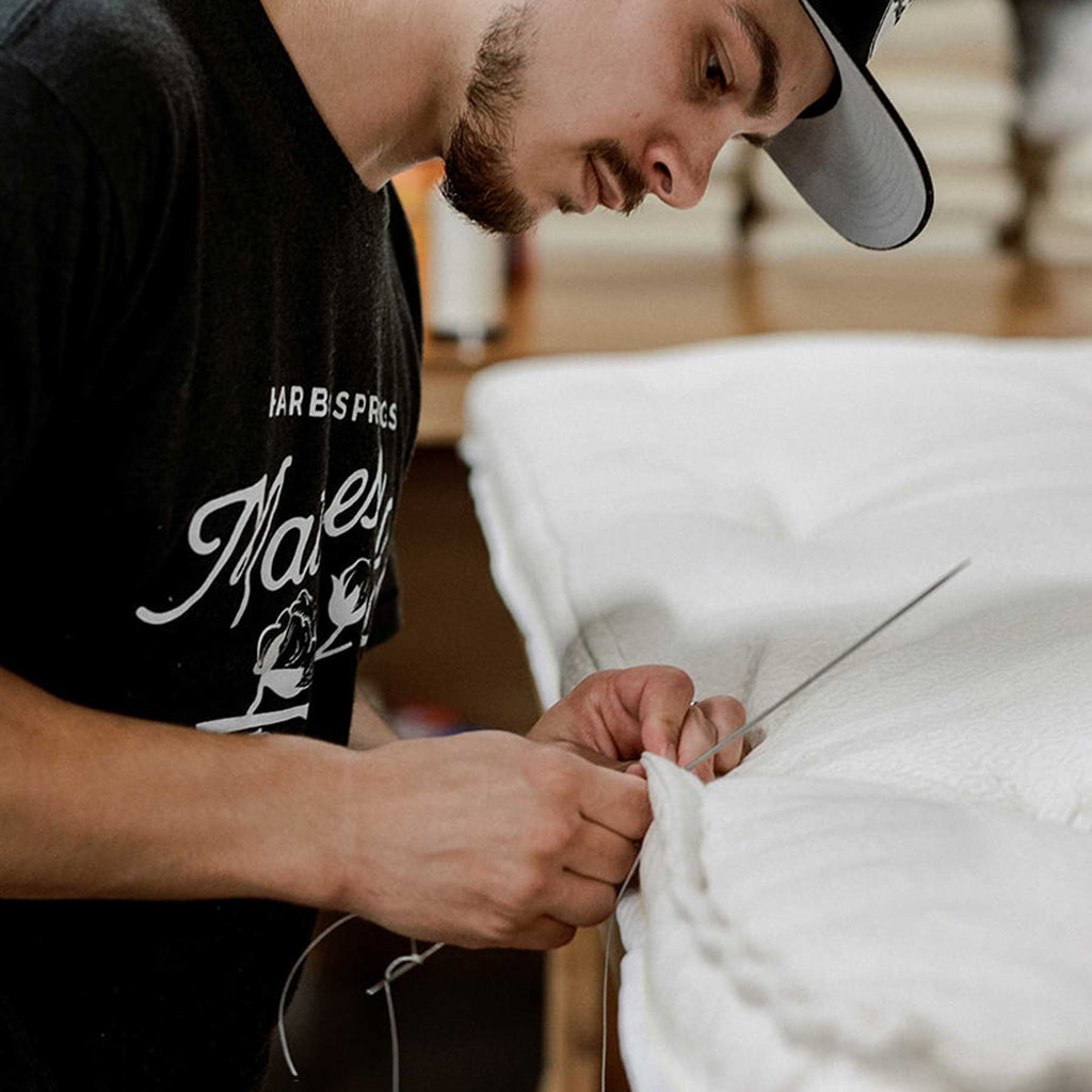 Craftsman hand stitching the sides of a luxury mattress.