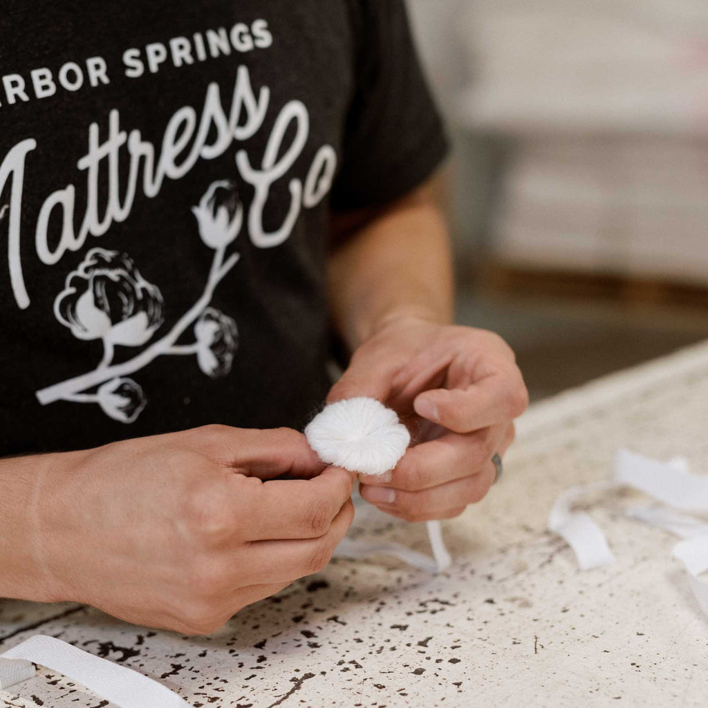 Craftsman assembling a wool rossette in preparation for needle-tufting a luxury mattress.