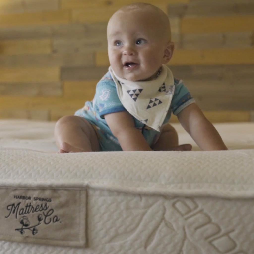 Baby sitting on a natural latex bed and smiling cutely.