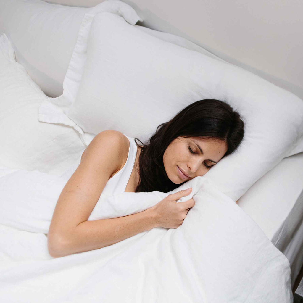 Woman looking very comfortable on a Harbor Springs Mattress dressed with white bedding.